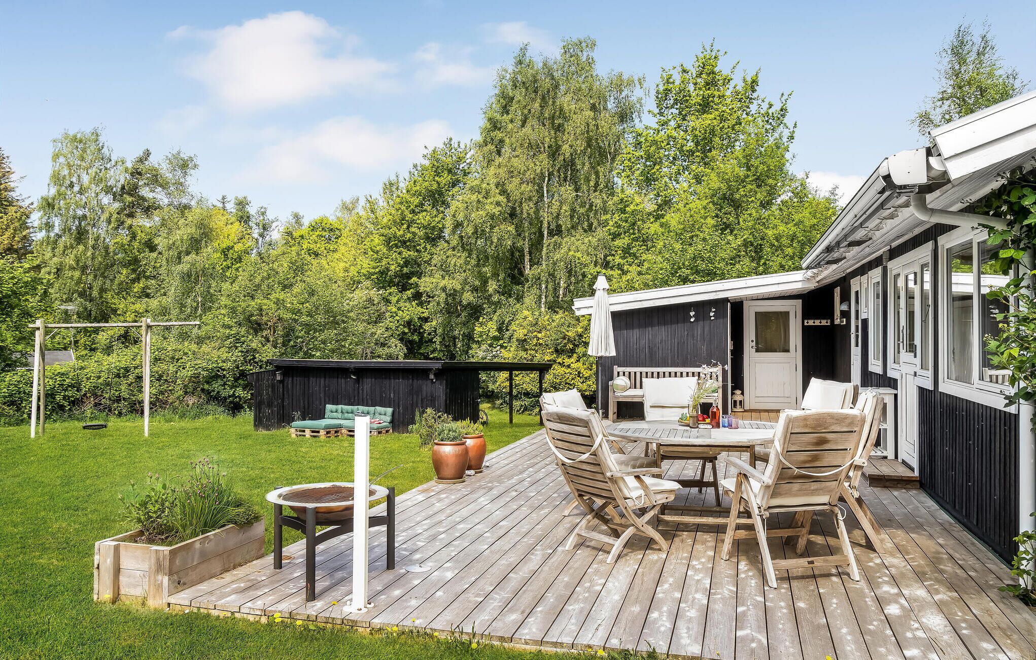 A wooden deck with outdoor furniture, a barbecue grill, and a garden area with a shed and greenery.