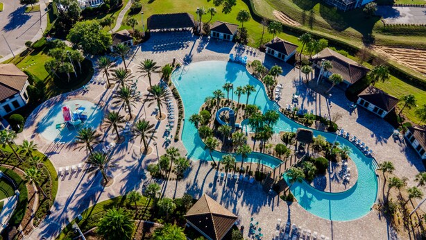Vista aérea de un resort con una amplia piscina serpenteante rodeada de palmeras y tumbonas.