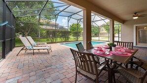 Un patio exterior con cerramiento de vidrio, suelo de ladrillo, piscina y una mesa de comedor para cuatro.