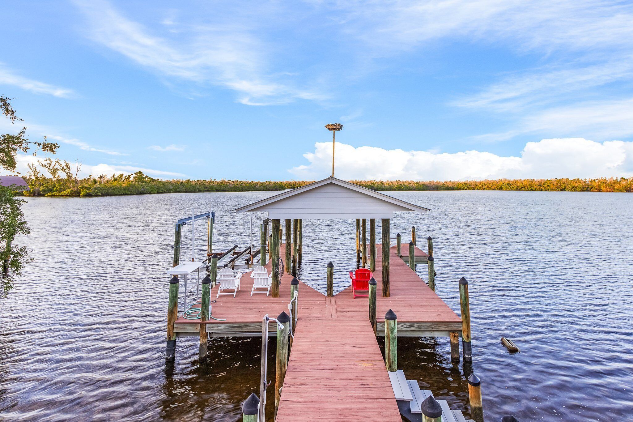 Eine hölzerne Pier mit überdachtem Bereich, weißen und roten Stühlen sowie einem Laternenpfahl.