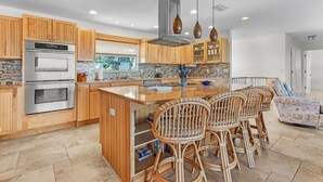 A modern kitchen with wooden cabinets, stainless steel appliances, a large island with bar stools, and pendant lighting. - Beautiful 5/3 Pool, Saltwater Cove, Sleeps 10! (Saint James City)