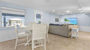 A modern living room with a dining area, a sofa, a TV, and a view of the outdoors. - Beautiful 5/3 Pool, Saltwater Cove, Sleeps 10! (Saint James City)