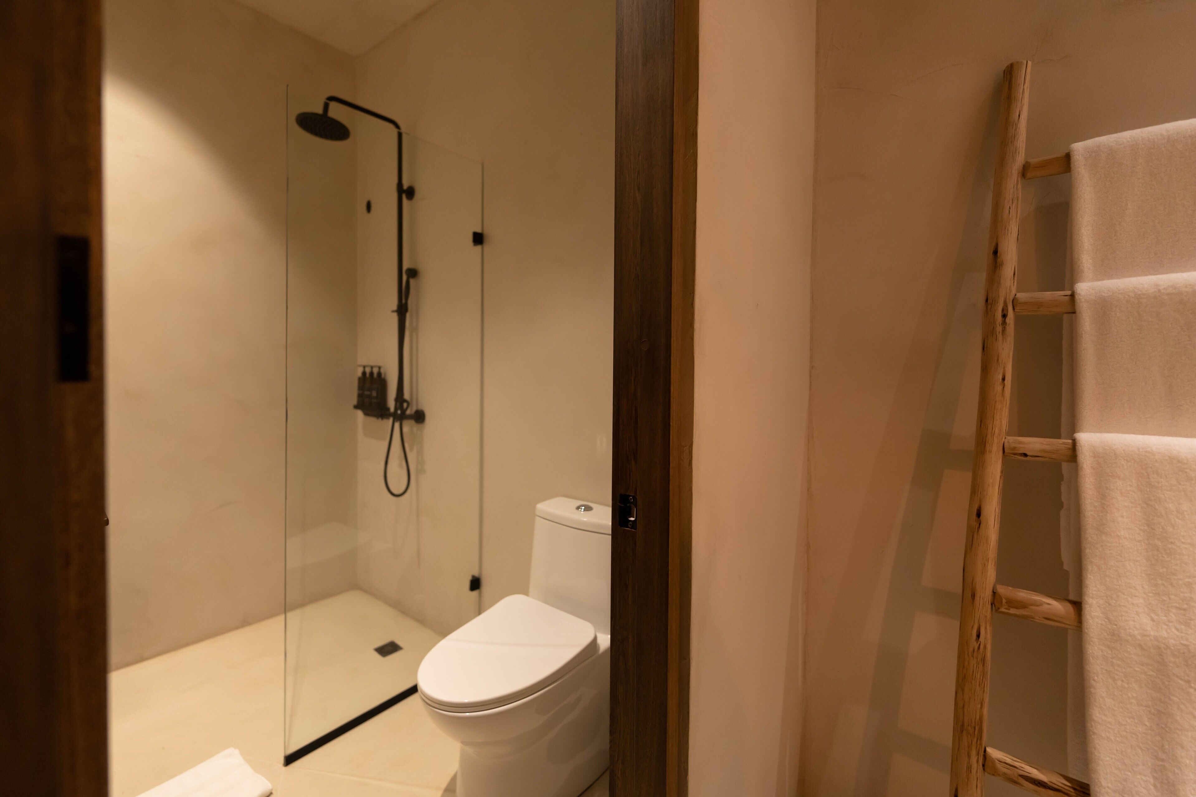 Un baño moderno con ducha acristalada, inodoro blanco y escalera de madera con una toalla.