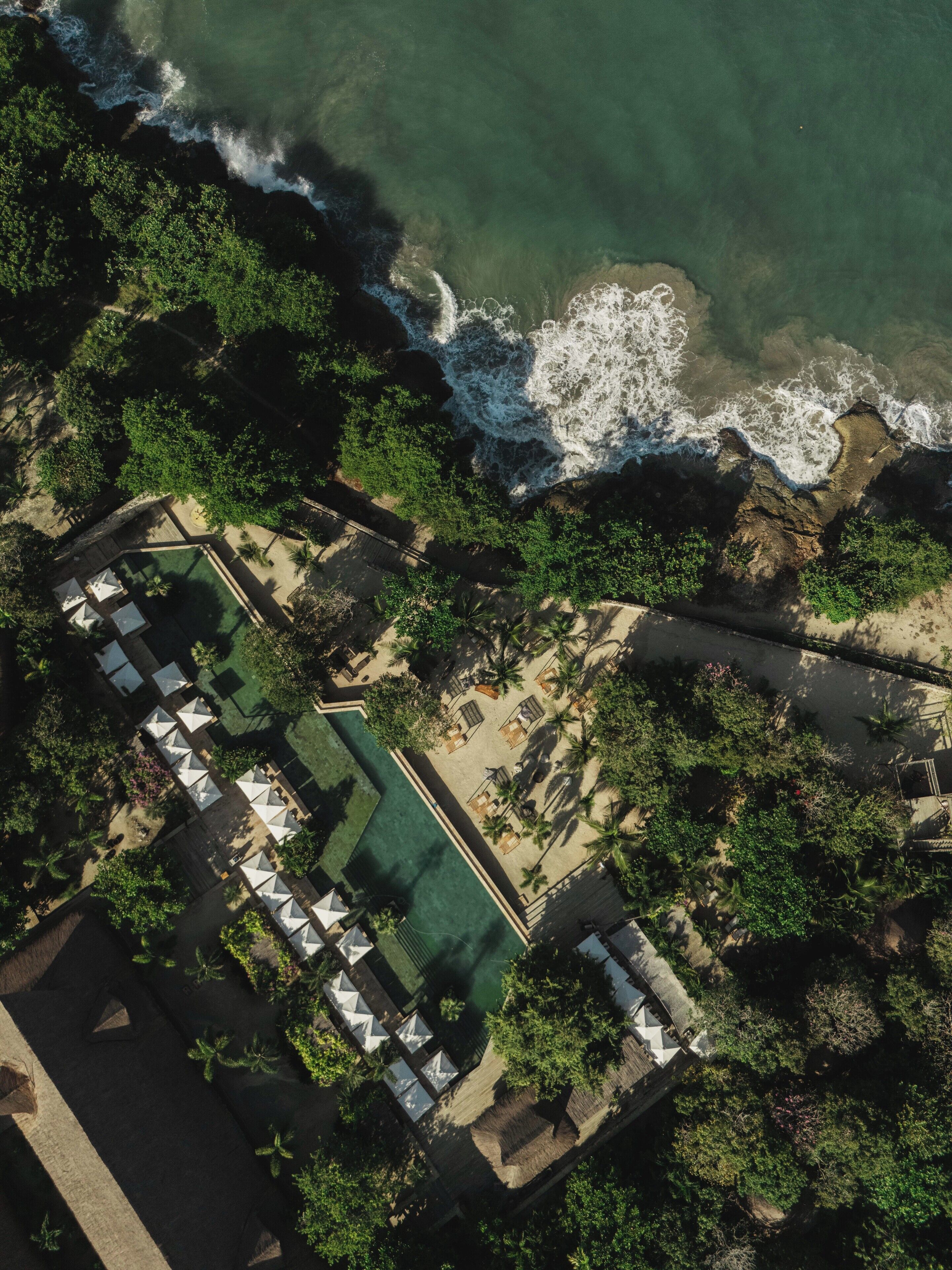 Vista aérea de un complejo turístico con piscina, zonas de descanso y playa.
