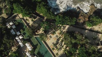 Vista aérea de un complejo turístico con piscina, zonas de descanso y playa.