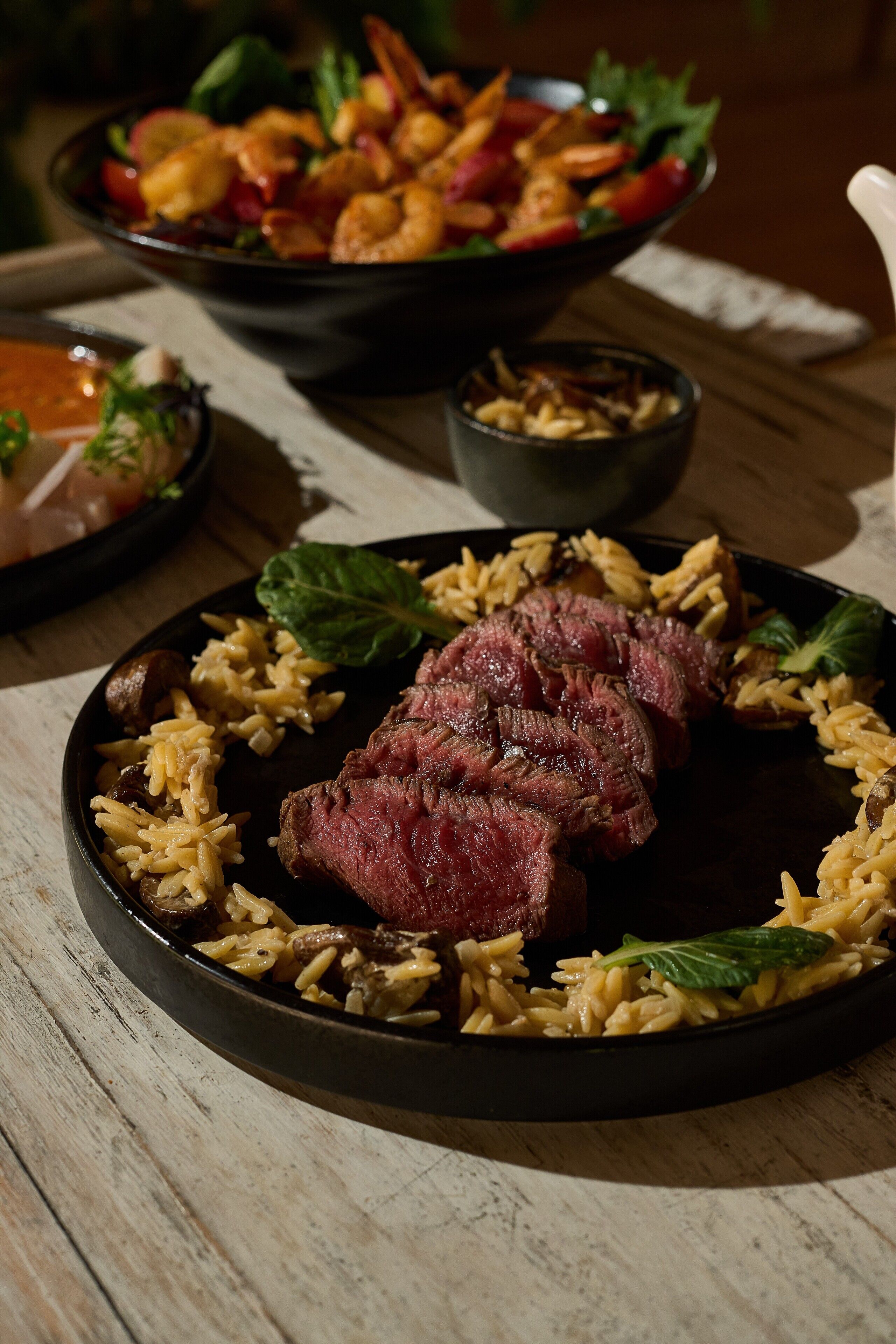 A plate of steak with mushrooms and rice, a bowl of shrimp salad, and a small bowl of sauce.