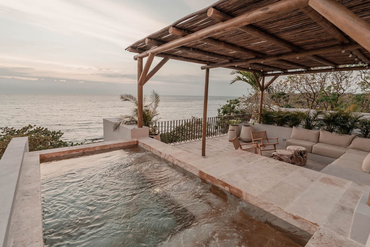A pool with a wooden pergola and outdoor seating area overlooking the sea.