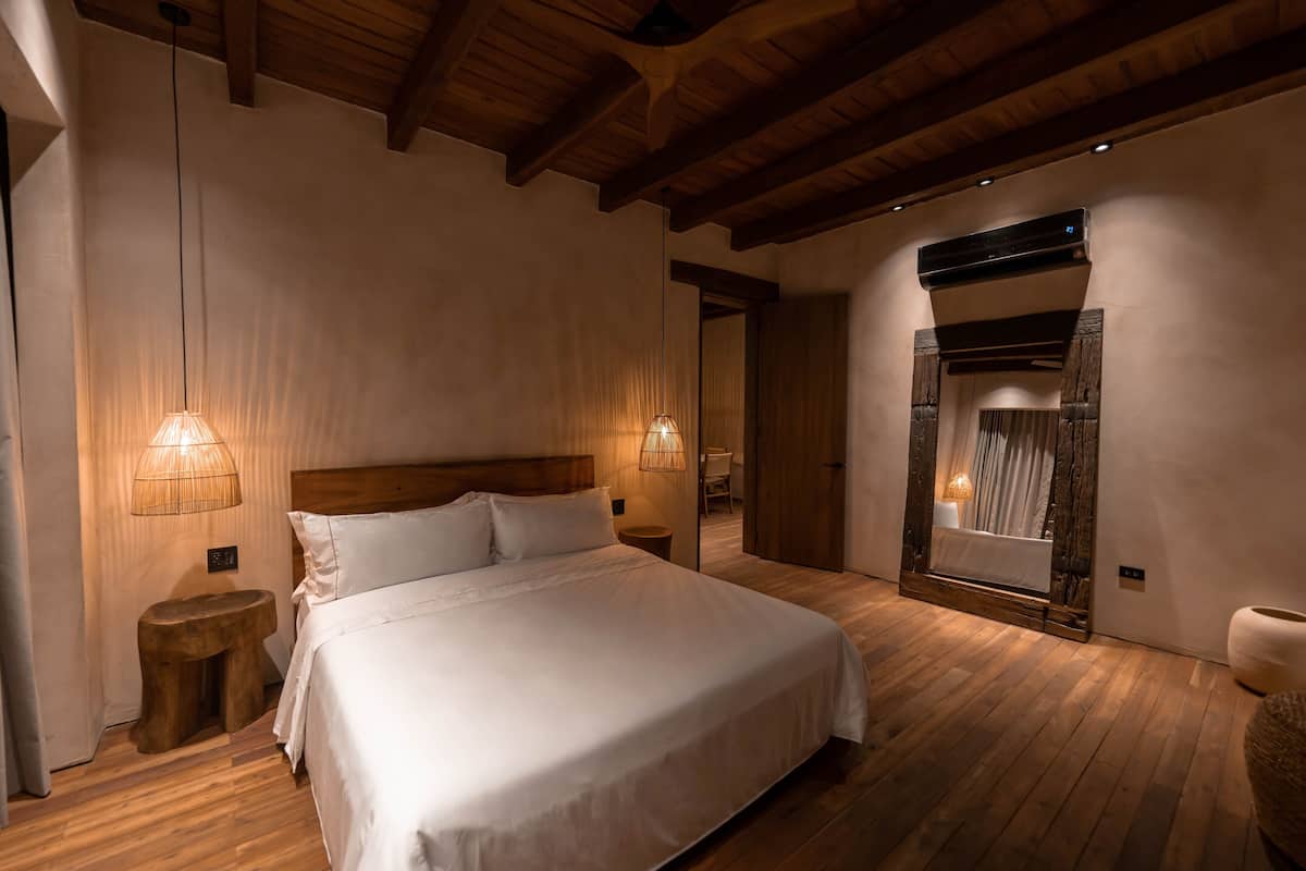 A bedroom with a large bed, wooden flooring, and a ceiling with exposed beams.