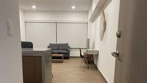 Een moderne, open woonruimte met een houten vloer, een grijze bank, een kleine tafel en een witte scheidingswand.