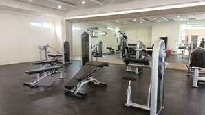 Een fitnessruimte met diverse trainingsapparatuur, waaronder banken en krachtapparaten, en een grote spiegel die de ruimte weerkaatst.