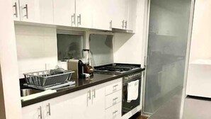 Eine moderne Küche mit weißen Schränken, einer schwarzen Arbeitsplatte und Edelstahlgeräten, darunter ein Herd und ein Backofen.