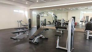 Ein Fitnessstudio mit unterschiedlicher Trainingsausstattung, darunter Bänke und Kraftgeräte, sowie ein großer Spiegel, der den Raum reflektiert.