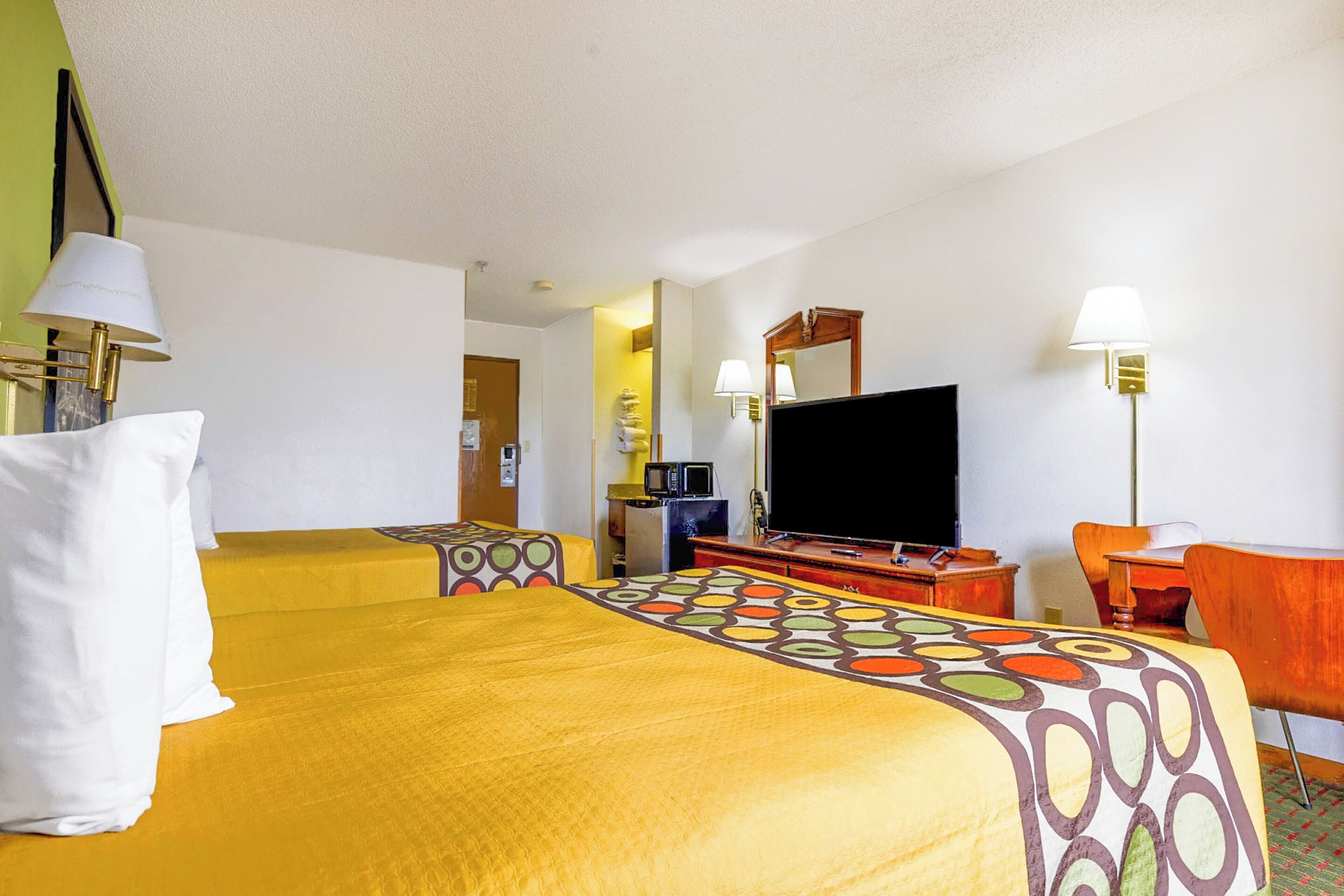 A hotel room with two beds, a television, a desk, and a chair.