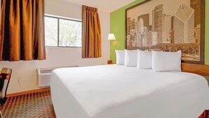 A hotel room with a large bed, a window with curtains, a cityscape painting on the wall, and a lamp on a nightstand.