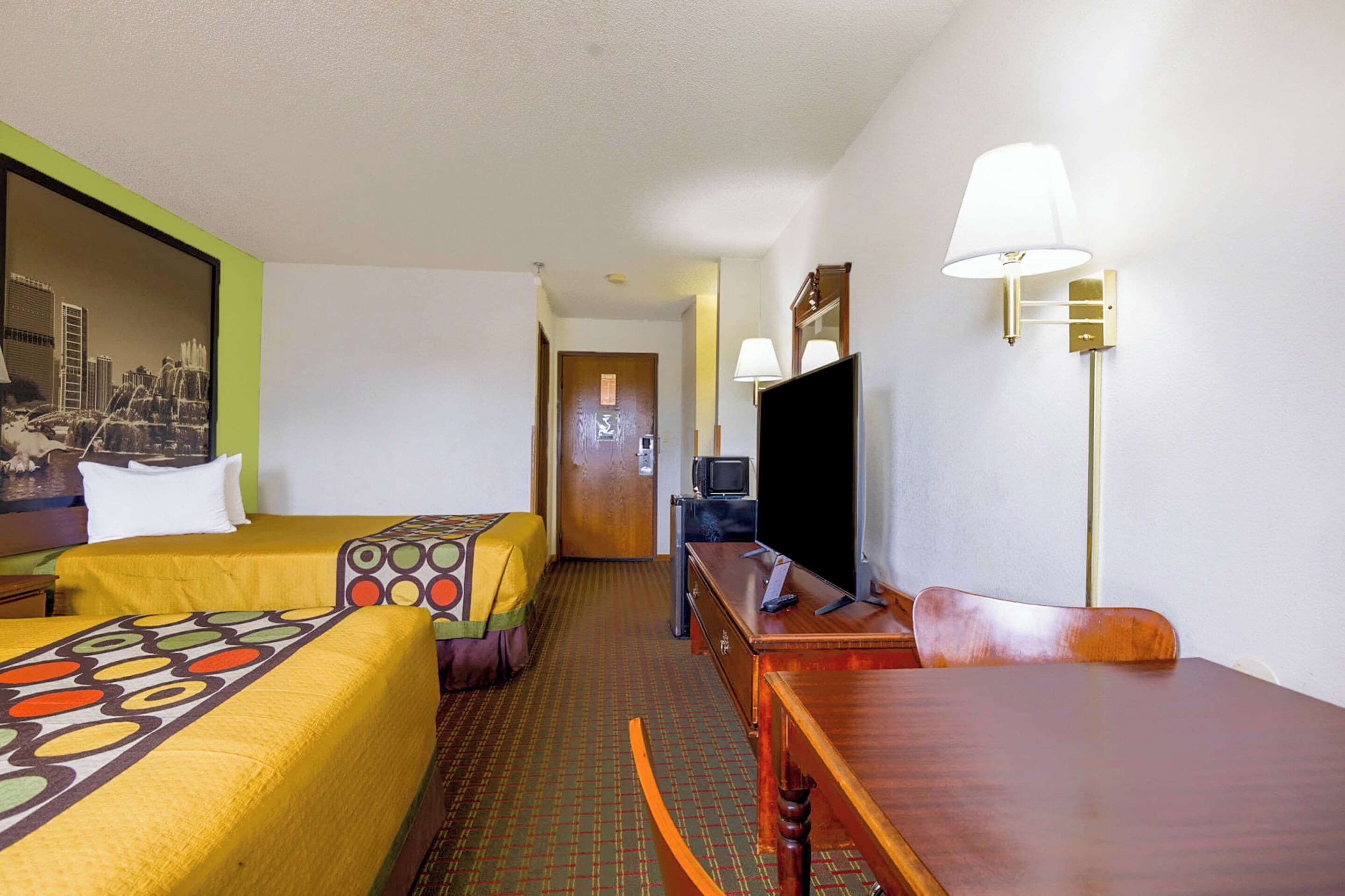 Ein Hotelzimmer mit zwei Betten, einem Schreibtisch, einem Sessel, einem Fernseher und einer Lampe.
