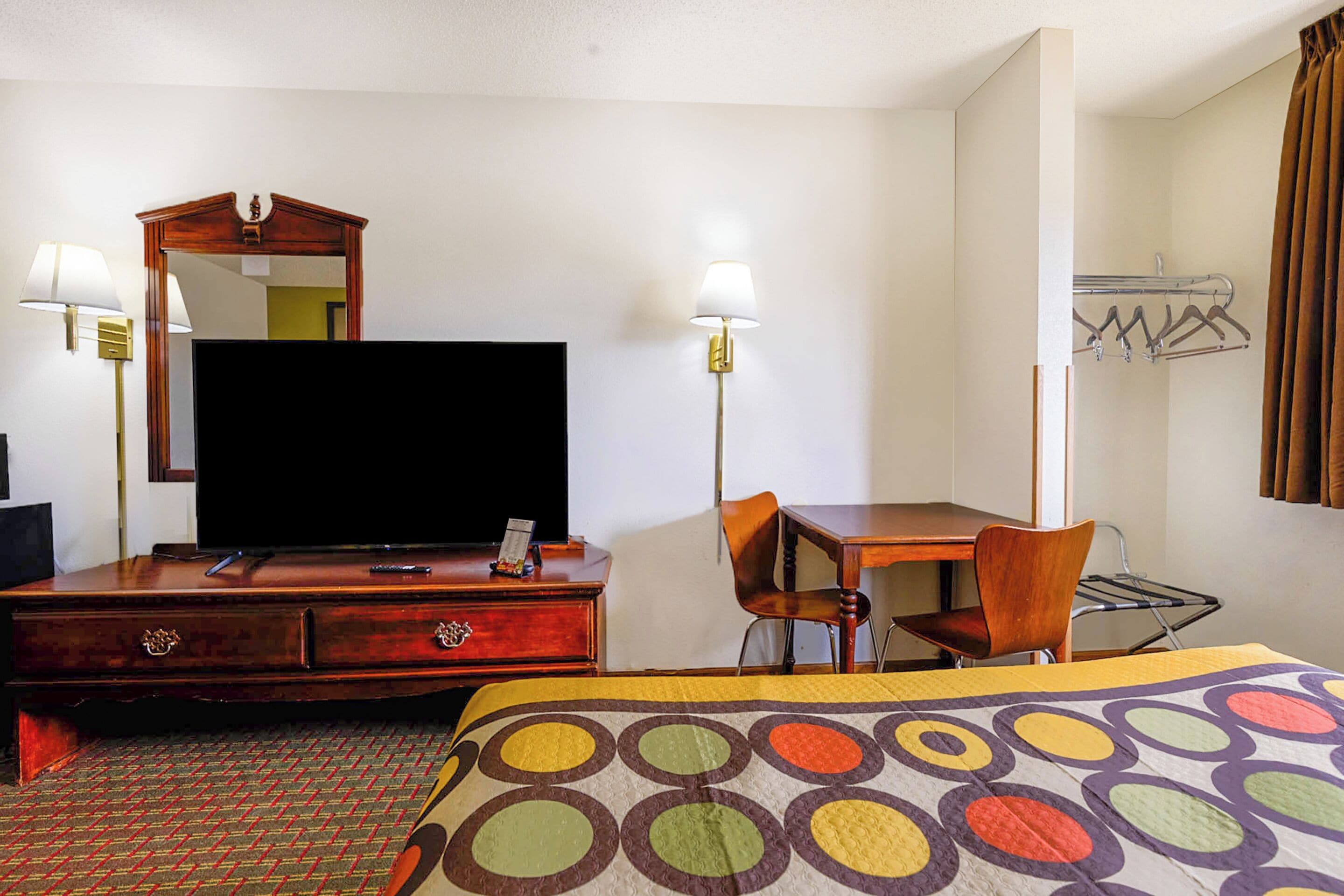 A hotel room with a bed, a desk, a chair, a television, a dresser, and a mirror.
