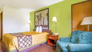 Habitación de hotel con cama, una silla, una mesita de noche, una lámpara y un cuadro en la pared.