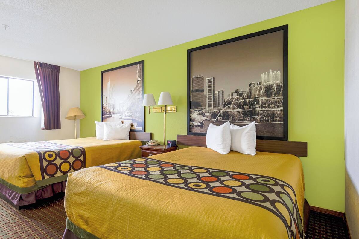 Quarto de hotel com duas camas, paredes verdes e uma grande pintura com vista para a cidade.
