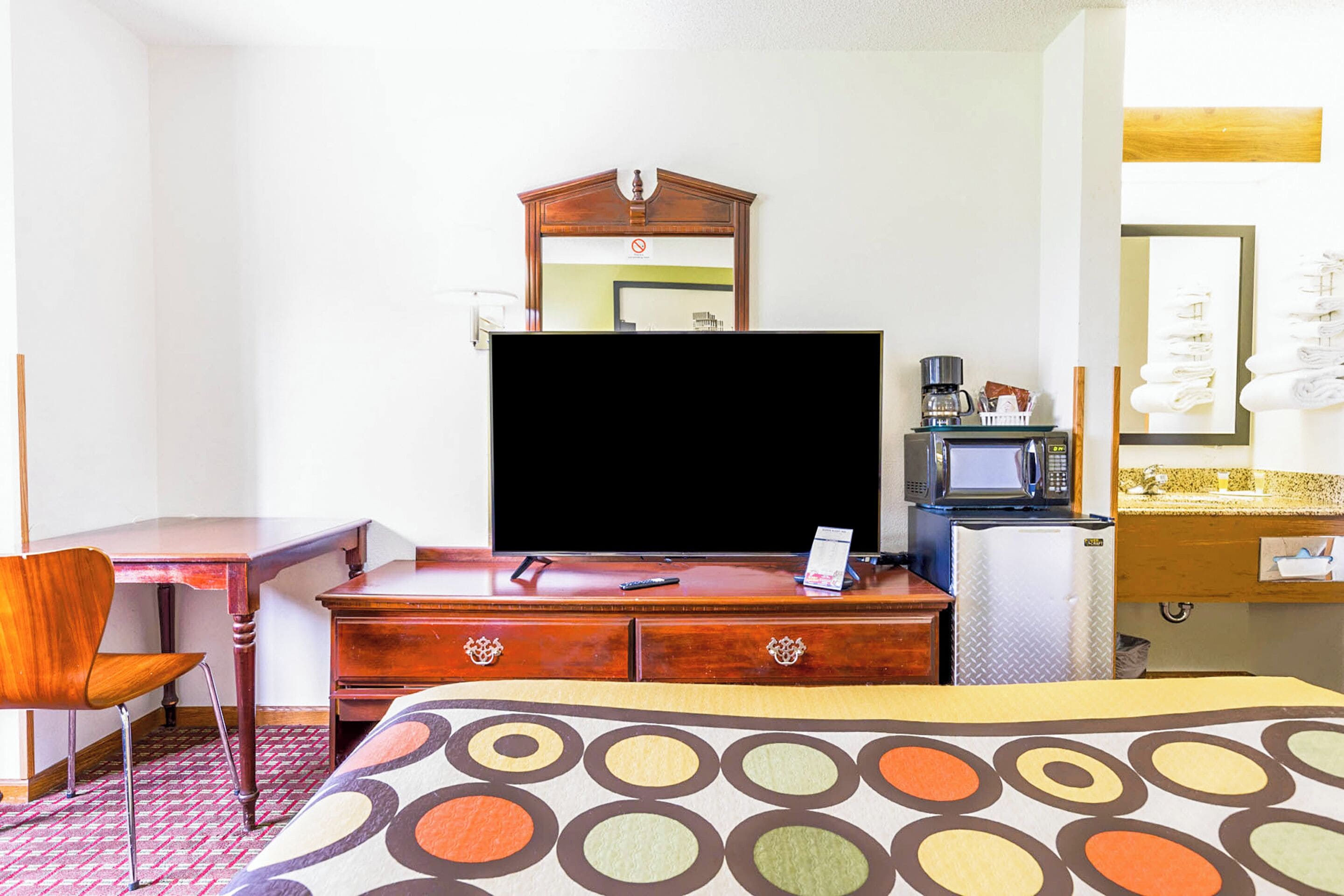 A hotel room with a bed, a desk, a dresser, a television, a microwave, and a mirror.
