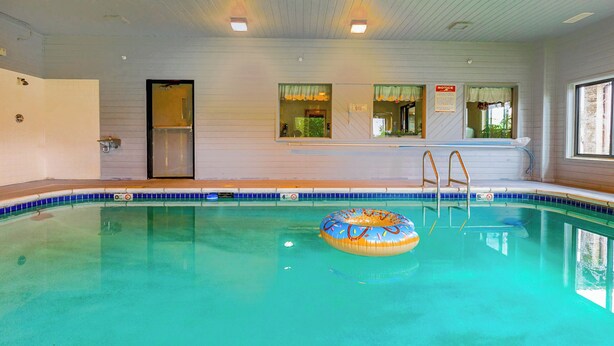 An indoor swimming pool with clear blue water, a ladder, and a colorful inflatable ring.