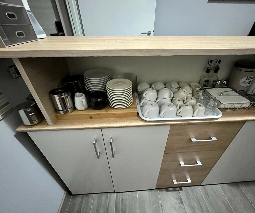 Eine Küche mit Holzausziehtisch, Spüle und Schränken. Auf der Arbeitsfläche stehen Stapel von Tellern, Schüsseln und Tassen.