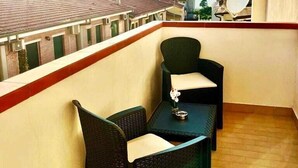 A balcony with two wicker chairs and a small table, overlooking a cityscape with buildings and a clear sky. - The Queen Tropea  (Tropea)