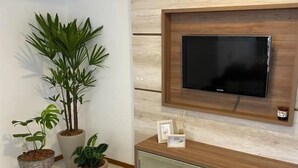 Una sala de estar moderna con un televisor de pantalla plana montado en una pared de madera, un aparador de vidrio debajo y varias plantas en macetas.