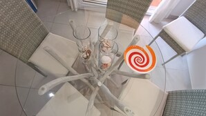 Un tavolo rotondo in vetro con una disposizione di sedie bianche, un bicchiere con una sostanza bianca e un piatto con un motivo a spirale rosso.