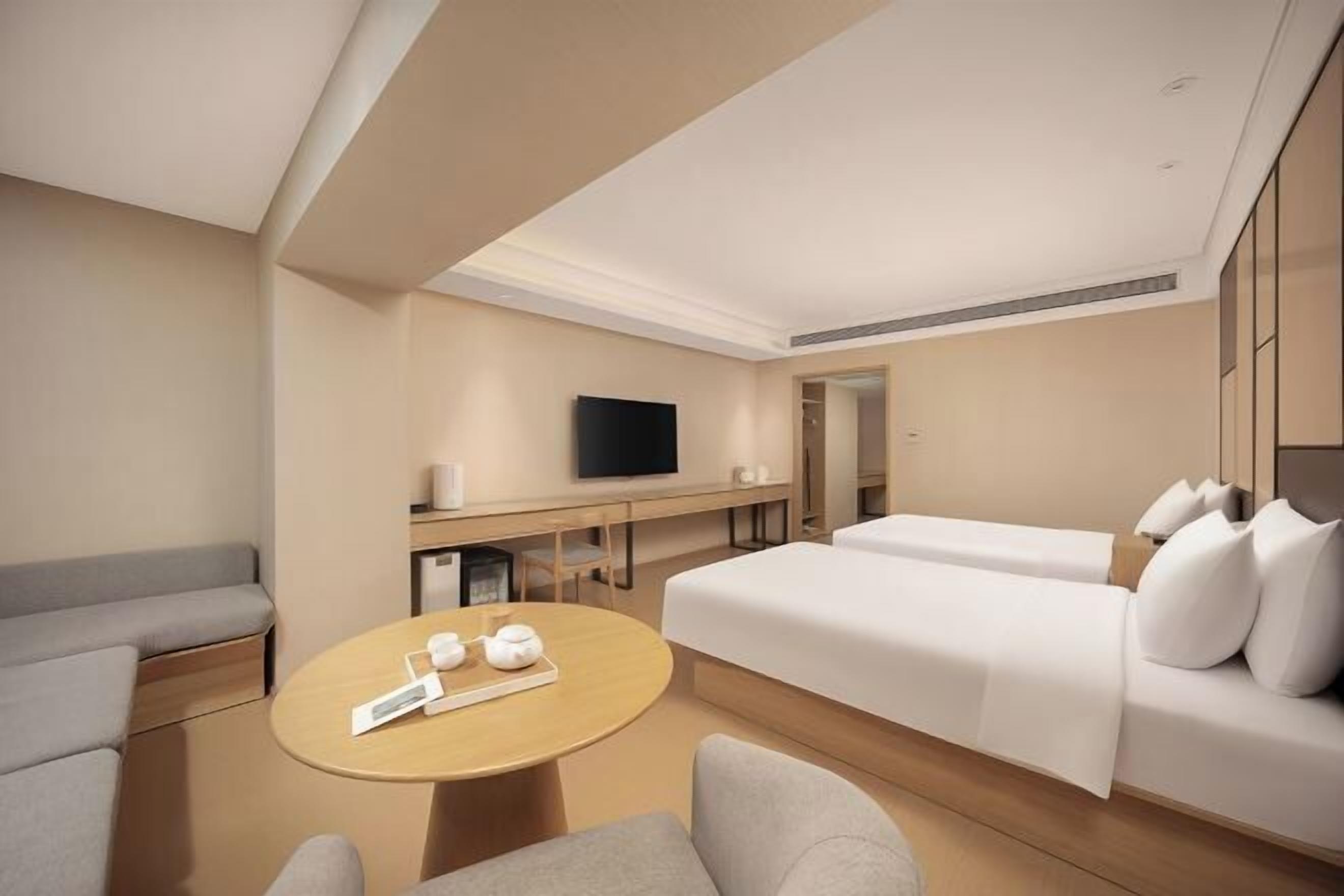 A modern hotel room with a sofa, a bed, a TV, a small table with a tray, and a mirror.