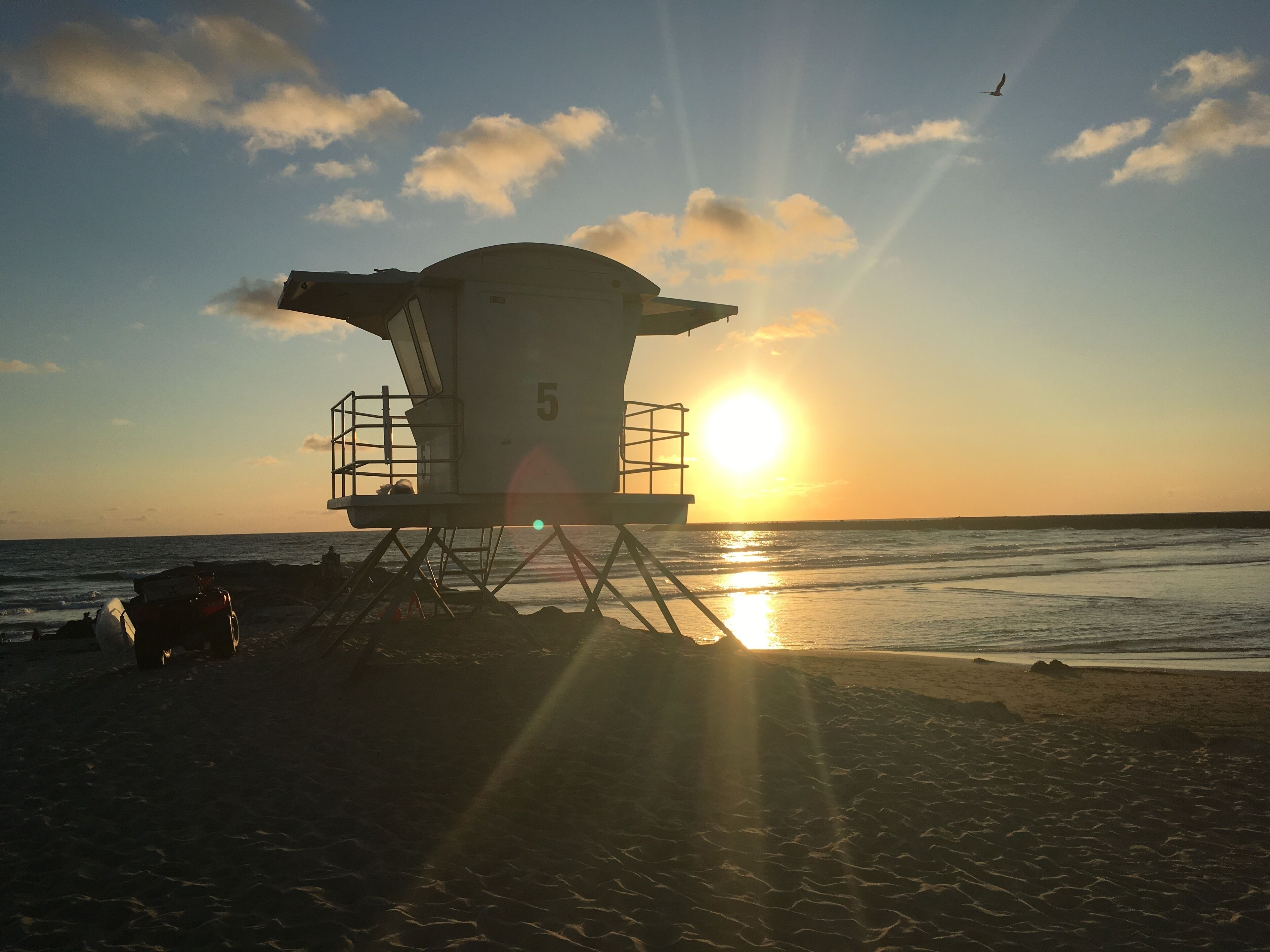 A lifeguard tower with the number 5 on it, located on a beach with the sun setting in the background.