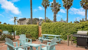 Outdoor seating with Adirondack chairs and picnic tables, a barbecue grill, and a hedge in the background.