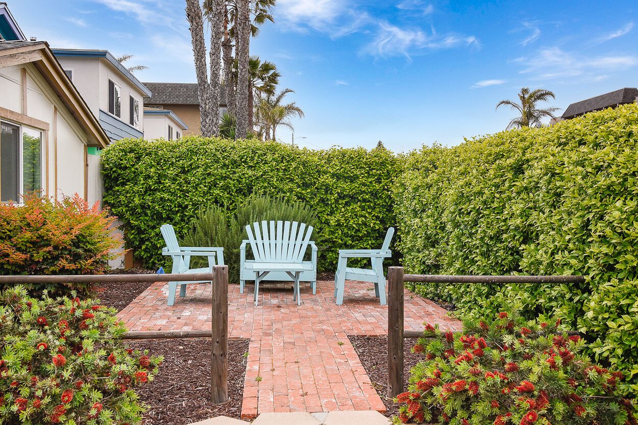A patio with two Adirondack chairs, a brick pathway, and a hedge.