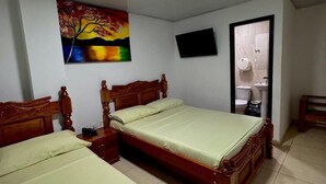 Un dormitorio con dos camas de madera, una lámpara en el techo, un cuadro, un televisor y una puerta de baño.