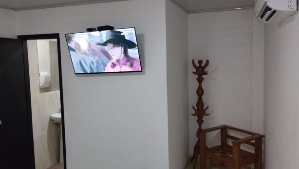 Una habitación con televisión montada en la pared, una silla de madera y una puerta que da al baño.