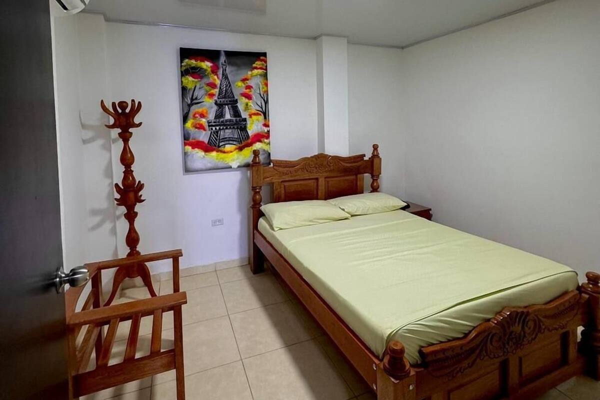 A bedroom with a wooden bed, a wooden chair, a painting of a tower, and a tiled floor.