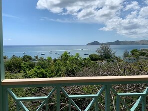 Blick vom Balkon auf eine Küstenlandschaft mit Booten auf dem Wasser und Bergen im Hintergrund.