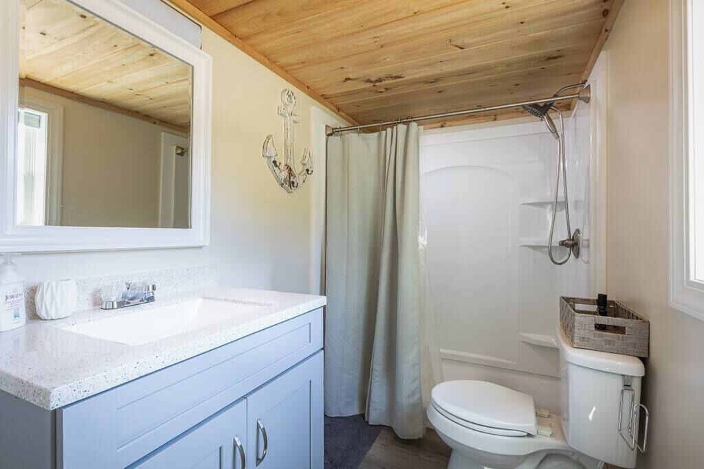 A bathroom with a wooden ceiling, a white sink, a toilet, and a shower area.