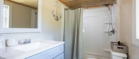 A bathroom with a wooden ceiling, a white sink, a toilet, and a shower area.