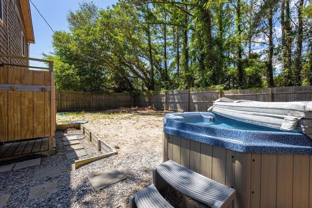 A backyard with a hot tub, wooden deck, and a wooden fence.