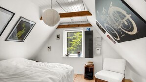 Een slaapkamer met een bed, een stoel, een raam met jaloezieën en kunstwerken aan de wanden.
