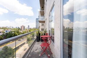 Un balcon avec une balustrade en verre, une petite table avec des chaises et des plantes en pot.
