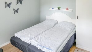Un lit avec une literie blanche, une tête de lit et une étagère ornée d’objets décoratifs.