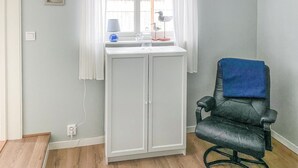 Une pièce avec un meuble blanc, une chaise noire sur laquelle est posée une serviette bleue, et une fenêtre avec des rideaux blancs.