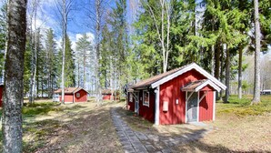 Punaisista mökeistä muodostuu rivi, ja kivipolku johtaa niihin. Mökit ovat korkeiden puiden ympäröimänä.