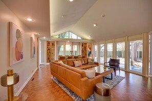Relax in this stylish living area with a large sofa, high ceiling, and floor-to-ceiling windows offering a view of the outdoors.