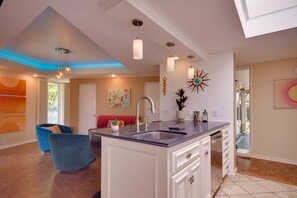 Kitchen features a central island with a sink, surrounded by cabinetry and a countertop, with pendant lights and a decorative wall piece.
