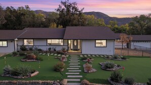 Une maison moderne à deux étages, dotée d’une pelouse bien entretenue, d’un chemin en pierre menant à l’entrée et offrant une vue sur les collines environnantes.
