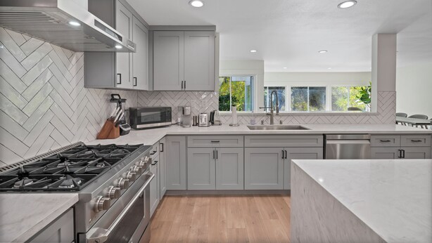 Une cuisine moderne avec des meubles gris, une cuisinière en acier inoxydable et un grand îlot central.