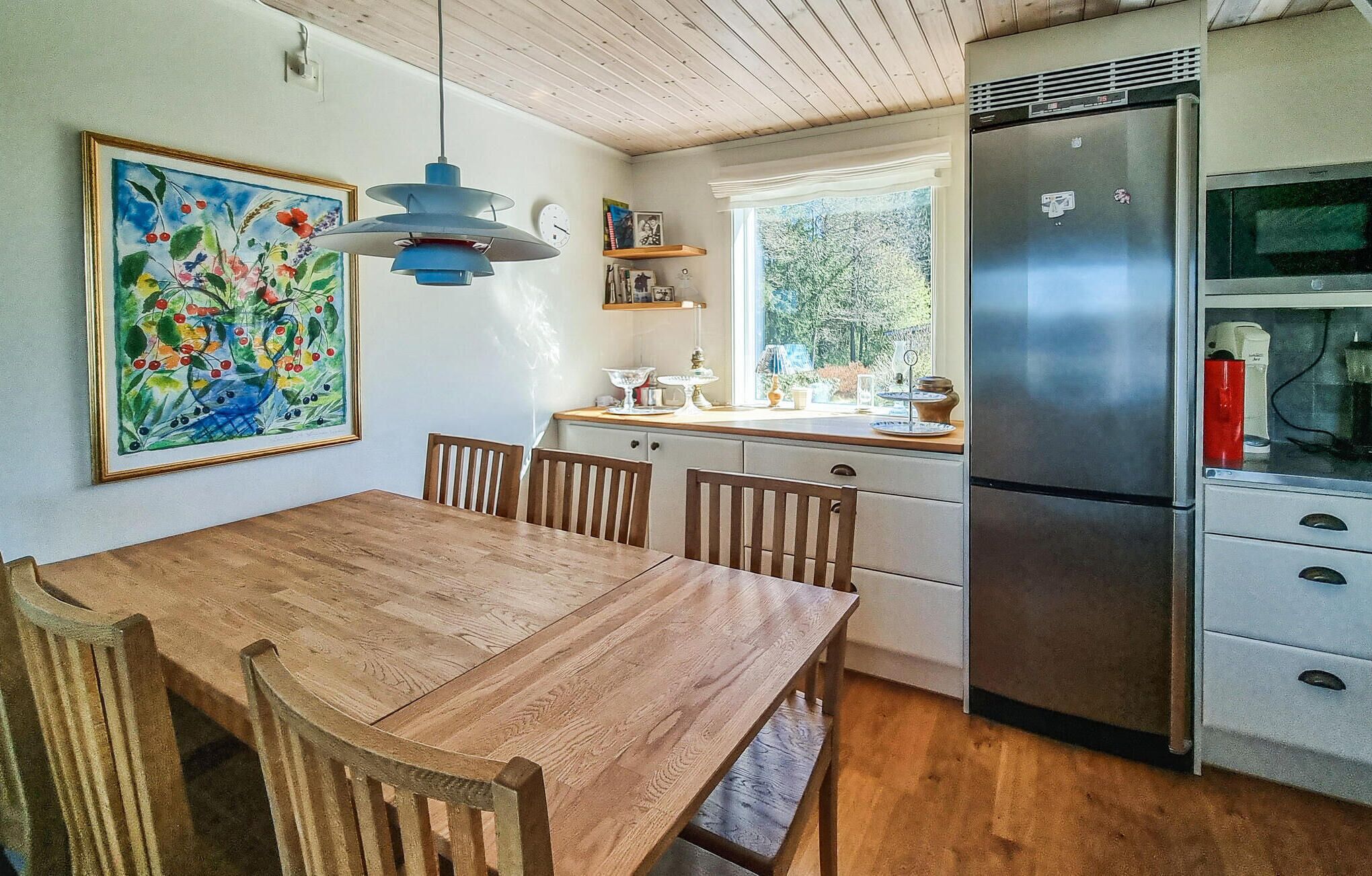 A kitchen with a wooden table, chairs, a refrigerator, and a window.