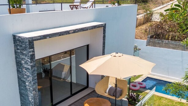 Ein modernes Haus mit einem Glasbalkon, Gartenmöbeln und einem Swimmingpool.